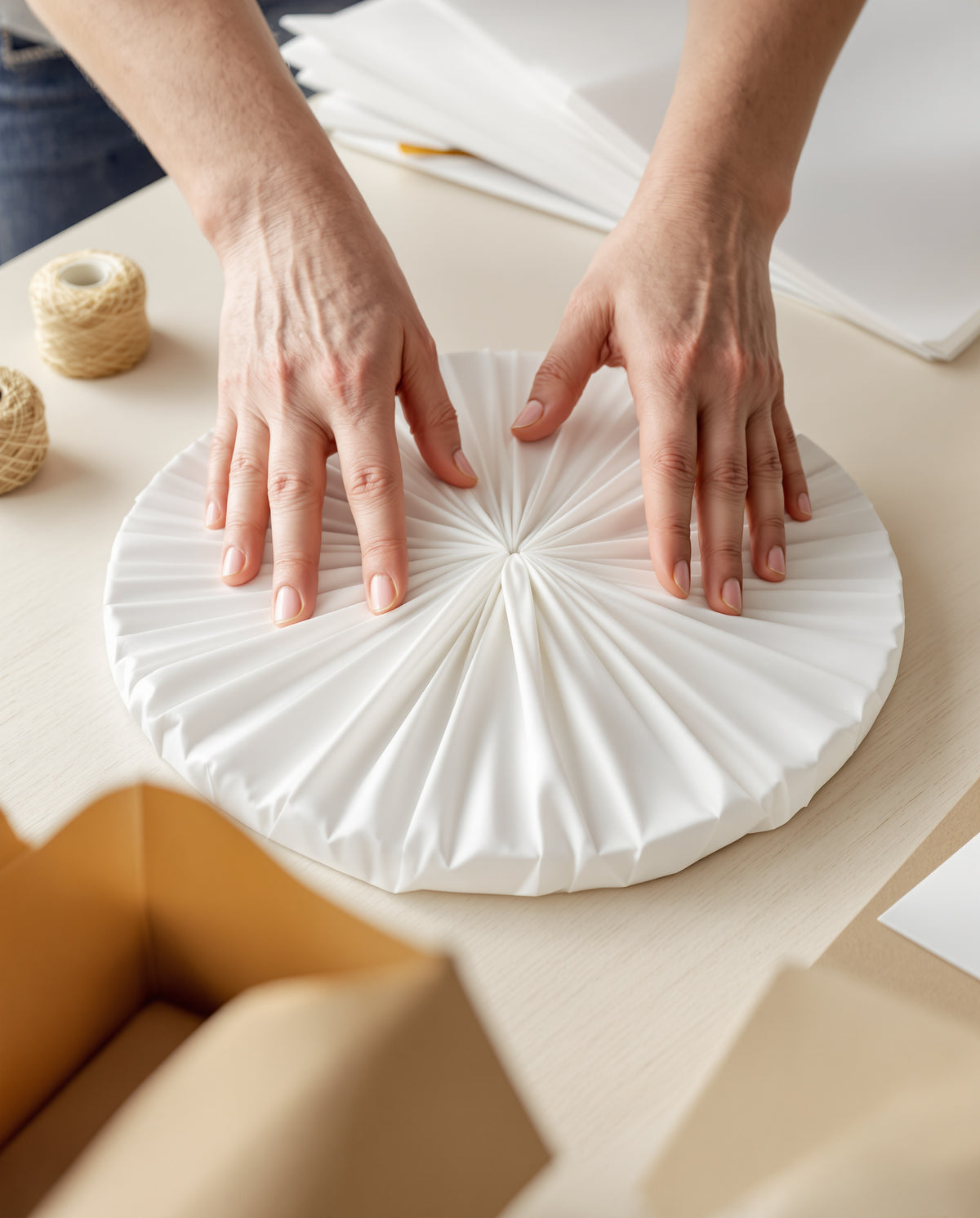 Hands wrapping a stoneware plate in soft protective paper at the packing bench